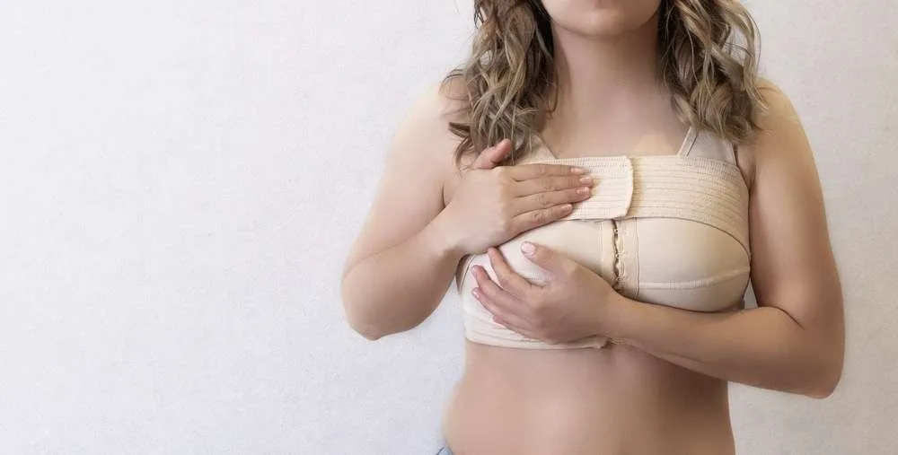 Young woman in beige compression bra bandage after breast augmentation surgery mammoplasty. banner. advertising. copy space