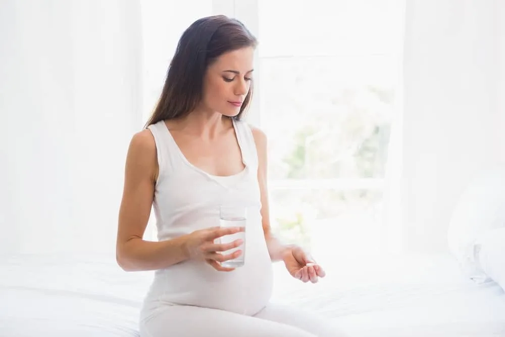 Pregnancy sitting on the bed taking a vitamin at home in bedroom