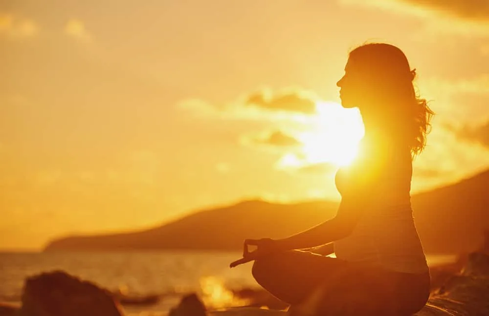 Pregnant woman practicing yoga in lotus position on beach at sunset
