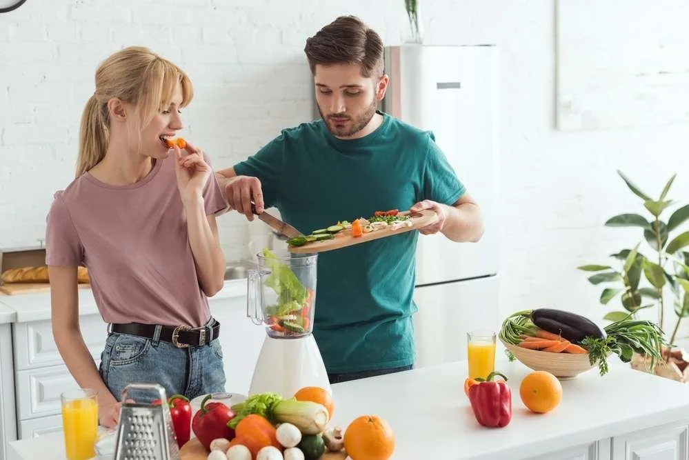 Young couple of vegans preparing vegetable juice at kitchen